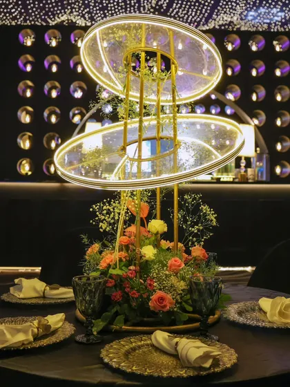 A stunning and modern centerpiece featuring illuminated rings and fresh flowers, perfectly complementing the monochrome theme with a pop of color.