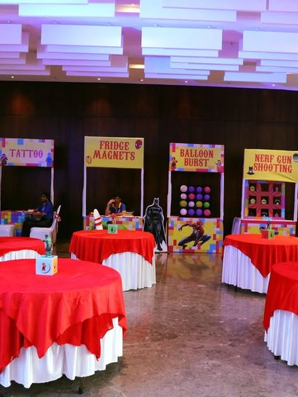 An overview of an indoor event space set up with various activity stalls. Each station, from tattoos to Nerf gun shooting, has its own themed banner and setup.