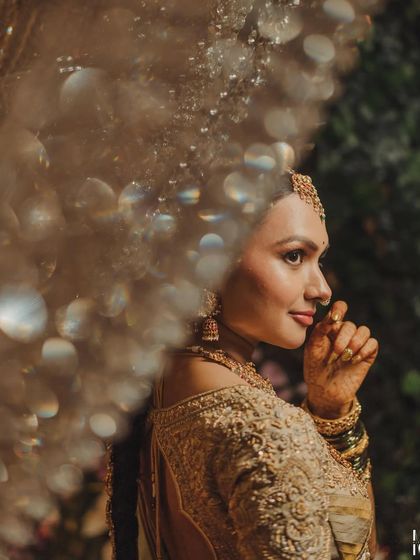 An artistic shot of a bride, with a crystal chandelier creating a beautiful bokeh effect. Her embroidered blouse and golden saree are the epitome of bridal luxury.