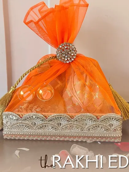 This vibrant orange Rakhi hamper is designed to be a bundle of joy. Wrapped in delicate organza with a sparkling centerpiece, it’s a beautiful way to present your love and festive treats for Raksha Bandhan.