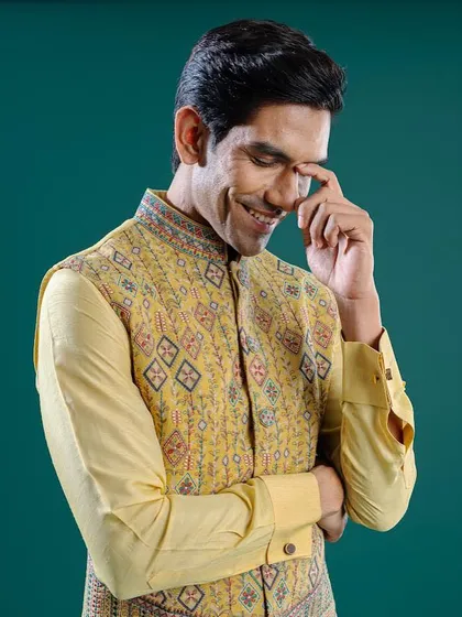 A smiling model wears a yellow Jawahar jacket with fine thread-work and a stunning color palette. This piece is designed to amp up your celebratory wardrobe.