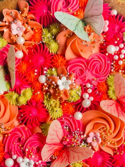 A close-up of the butterfly tart, showing the rich pink and orange tones of the buttercream and the delicate, life-like details of the edible butterflies.