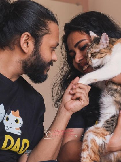 A beautiful family portrait with their calico cat, Hermione. The "Cat Dad" shirt and the gentle way they hold her paw tells a story of a truly cherished pet.
