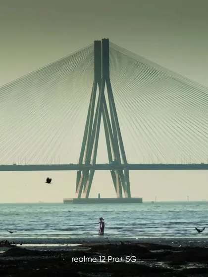 A beautifully framed shot of the Bandra-Worli Sea Link, captured on a mobile phone. The composition with the person in the foreground adds a sense of scale and human element to the grand structure.
