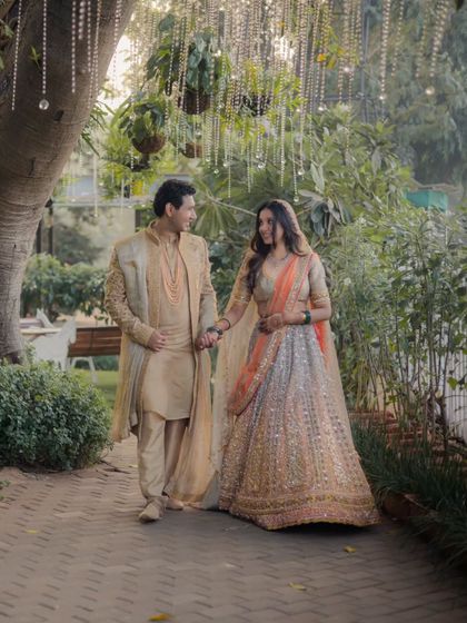 The couple walks hand-in-hand through a beautifully decorated garden path, a perfect portrait from their sundowner wedding.