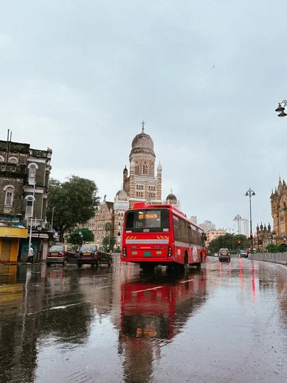 A red BEST bus makes its way down a wet street, with the historic BMC building in the background. The reflections on the road are what make these cityscapes so dynamic.