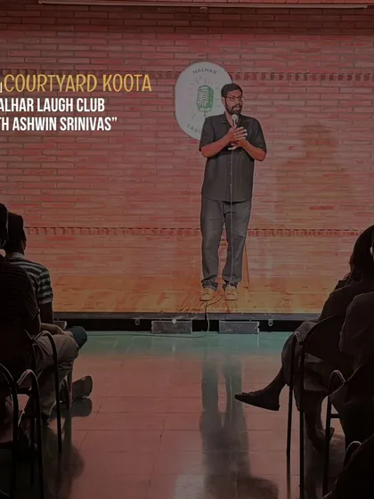 A shot of Ashwin Srinivas on stage during his show for Malhar Laugh Club, with our signature brick wall and MLC logo in the background.