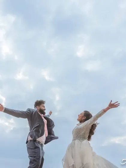 A dynamic shot of the couple jumping for joy against the sky. Their energetic pose and happy expressions convey a sense of pure excitement and fun.