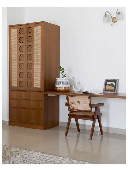 A pooja mandir subtly tucked into the corner of the guest bedroom. The unit features cane shutters with carved temple flowers for ventilation and extends into a sleek study table.