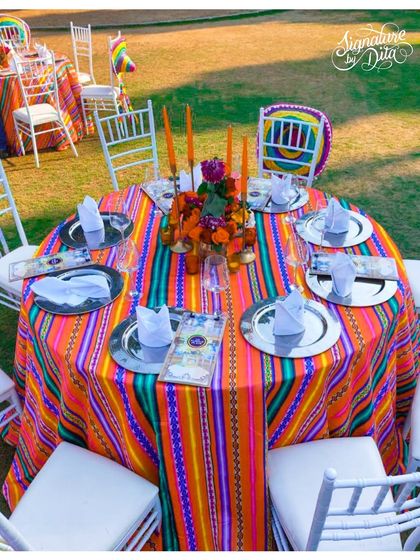 A tablescape from the Mexican fiesta, featuring a brightly striped tablecloth, silver charger plates, and a centerpiece of orange candles and flowers.