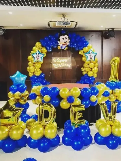 A Mickey Mouse themed first birthday party with a blue and gold balloon arch and name display.