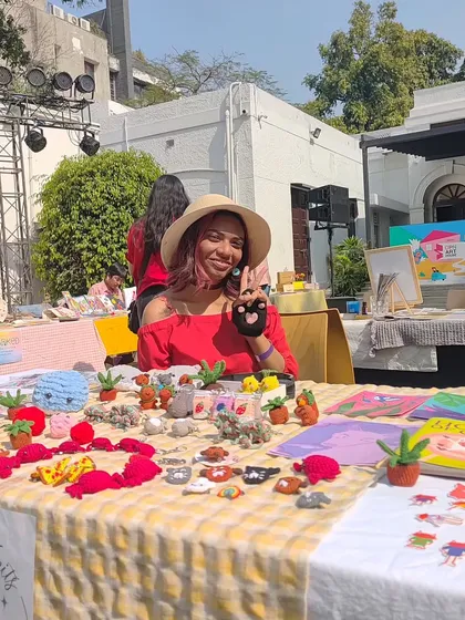 This is me at my stall during a weekend art market. I love getting to meet everyone and share my work. You can see my table full of colorful cross-stitch and crochet creations, from tiny plants to cute animal charms.