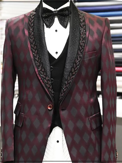 A three-piece tuxedo in a deep burgundy with a black diamond pattern. The lapels are embellished with intricate beadwork, adding another layer of luxury.