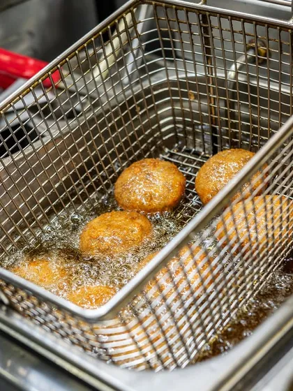 Golden-brown appetizers fresh from the fryer. The bubbling oil and crispy texture are the focus of this action-oriented kitchen shot.