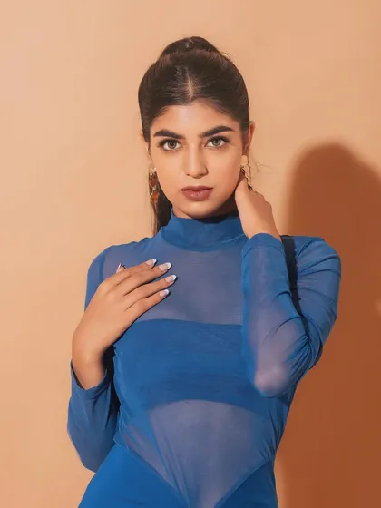A powerful and confident pose. The makeup is kept clean and minimal, with a focus on a strong brow and a defined lip, complementing the bold blue dress. slight blush and a berry-toned lip.