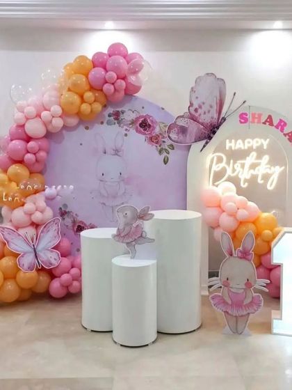 A sweet and simple bunny and butterfly theme perfect for a first birthday. This setup uses a soft color palette, a custom arched backdrop, and a neon 'Happy Birthday' sign for a modern touch.