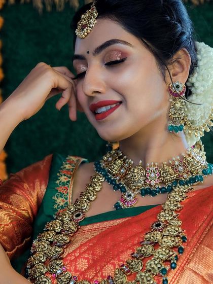 A beautiful close-up of a model wearing a grand temple jewellery set with green bead accents. The intricate details of the choker and haram are stunning.
