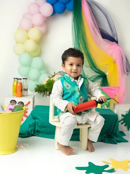 Ready to play with colors. This little boy is all set for his first Holi photoshoot with a pichkari and a colorful, festive outfit.