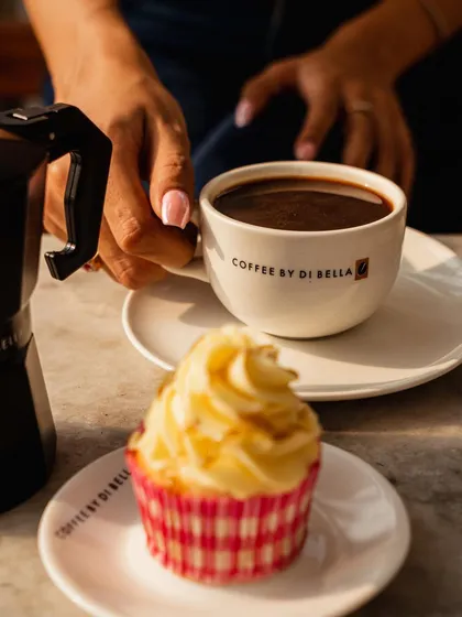 This shot creates a perfect pairing of coffee and a sweet treat. The lifestyle element of a hand reaching for the cup makes the scene feel warm, personal, and inviting.