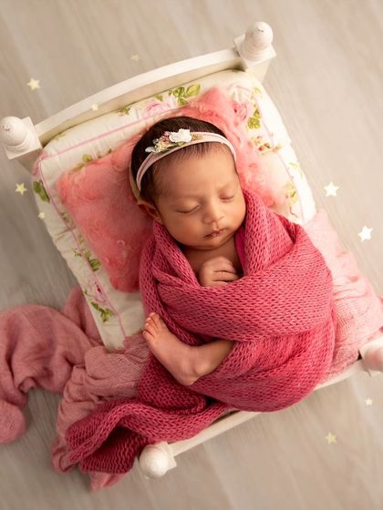 Sweet dreams are made of this. A baby girl is wrapped snugly in pink on a floral-patterned miniature bed, with a soft, dreamy edit that adds a touch of magic.