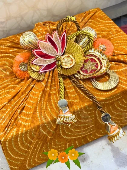 A gift box wrapped in vibrant yellow bandhani fabric. The top is adorned with a stunning, handcrafted lotus motif made from gota patti, showcasing my love for traditional Indian crafts.