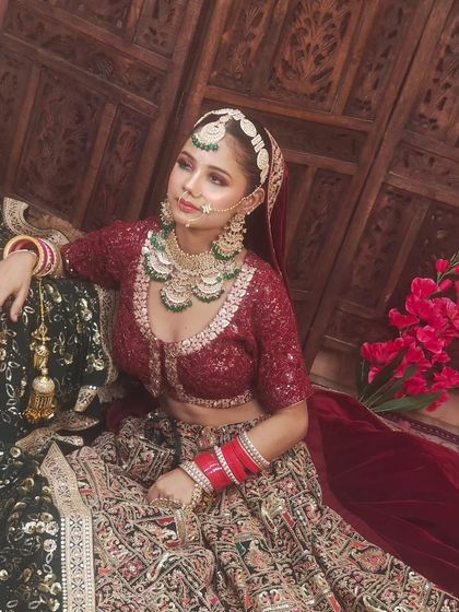 A bride seated in a dark green and red lehenga with intricate embroidery. The velvet blouse adds a touch of luxury to the outfit.
