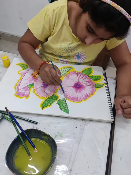 A young student carefully paints a floral composition, learning to control the water and pigment to create soft, blended colors.