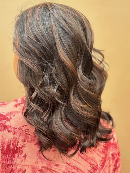 A close-up back view of a client's hair, showing the delicate blend of highlights. The wavy style adds texture and movement, creating a beautiful, natural look.