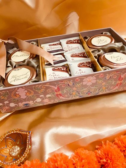 A beautifully patterned box designed to hold a variety of treats. This Diwali hamper includes almond brittle and four jars for makhana, dry fruits, and more.