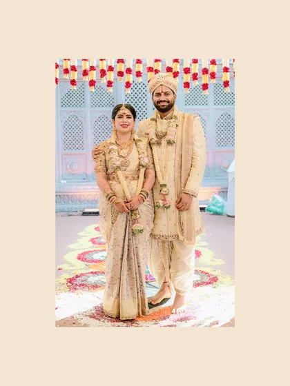 A full-length portrait of the couple. The groom's bespoke sherwani, dhoti, and shawl are perfectly coordinated, creating a harmonious look for their wedding album.