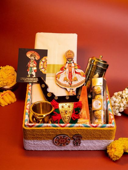 The 'Kasavu & Katha' hamper, fully assembled in its colorful, thread-wrapped box. This gift combines textiles, brassware, and decor to create a rich tapestry of Kerala culture.