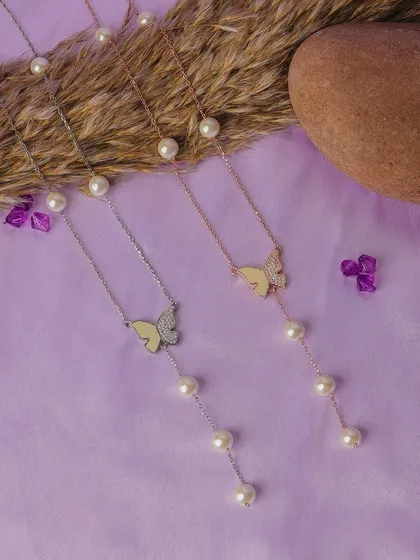 This is a clean and elegant e-commerce product shot, styled to highlight the delicate design of these butterfly necklaces. The soft lavender background and natural elements make the jewelry pop, perfect for an online catalog.