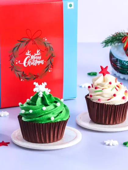 Our Christmas cupcake gift boxes are a perfect festive treat. This set includes a Christmas tree cupcake with green frosting and a classic vanilla cupcake with red and white sprinkles, ready to be gifted.