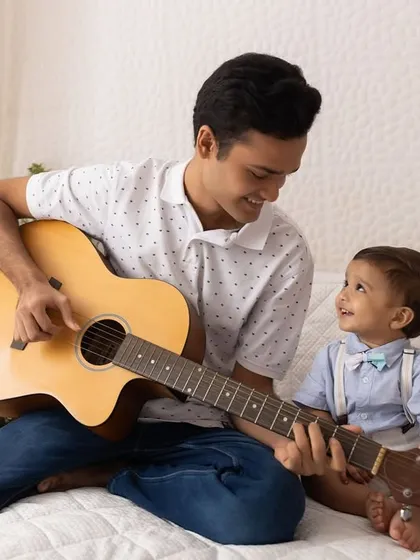 A special bond between brothers. An older brother plays the guitar for his fascinated baby brother during a lifestyle session.