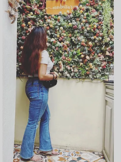 A back-facing shot of me admiring a beautiful flower wall at a picturesque cafe, perfect for creating aesthetic, Instagrammable content.
