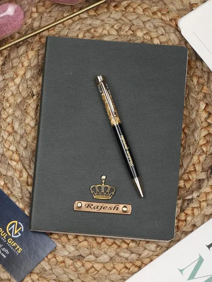 A personalized black leather diary with a crown charm, paired with a gold flake pen, creating a classic and timeless gift set.