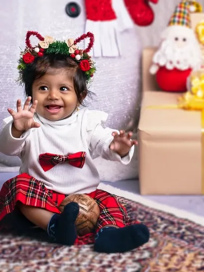This little one, with her festive reindeer headband, is waving hello to the magic of Christmas, surrounded by beautifully wrapped gifts.