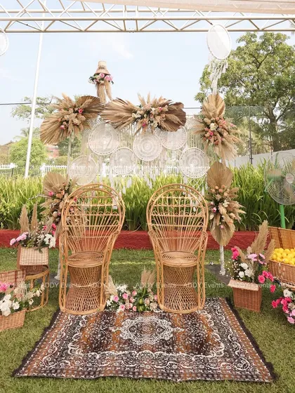 A unique Haldi or Mehndi seating arrangement featuring rustic rattan peacock chairs, a patterned rug, and bohemian accents like dreamcatchers and pampas grass.