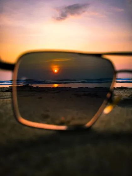 Reflecting on a beautiful sunset. This photo captures the setting sun reflected in a pair of sunglasses on the sand, offering a unique and personal view of a classic beach scene.