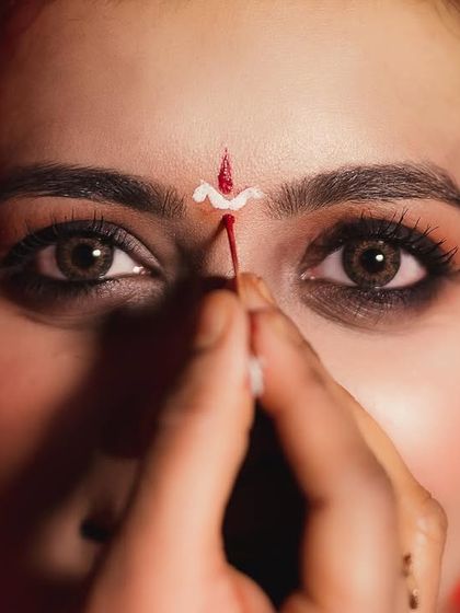 A detailed macro shot focusing on the makeup artist applying the traditional bindi to the bride's forehead. The intensity in her eyes makes this a powerful and intimate getting-ready photo.