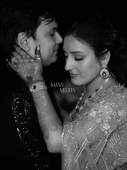 A stunning black and white close-up capturing a moment of intense connection during a Sangeet night. The focus on the bride's henna-adorned hand gently caressing his face is incredibly powerful.