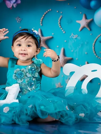 Celebrating her first birthday with an under-the-sea mermaid theme. The teal dress and ocean-inspired backdrop are perfect for a little princess.