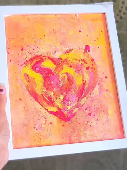Holding the joyful pink and yellow heart. The white frame keeps it feeling fresh and modern. This piece is like a burst of sunshine, perfect for brightening up any room.