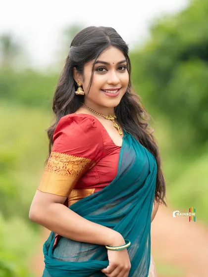 A smiling portrait of a model in a teal and red half saree. The outdoor lighting and her cheerful expression create a fresh and vibrant look.