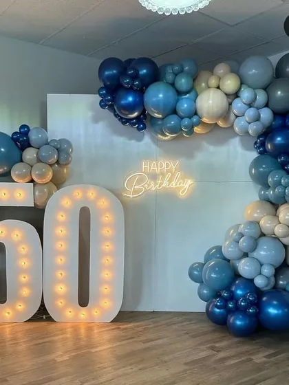 Celebrating a 50th birthday in style with large marquee numbers and a sophisticated organic balloon garland in shades of blue, grey, and beige. A warm neon sign adds a personal touch to this milestone event.