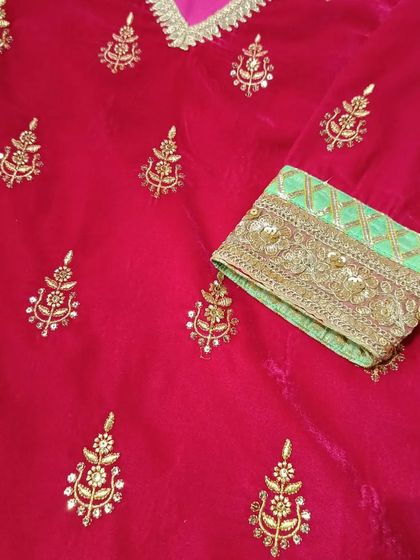 A close-up of the intricate gold hand embroidery on the sleeve and body of the red velvet kurta.