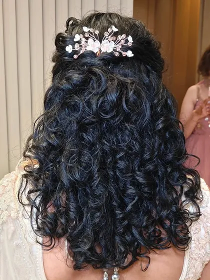 This bride's reception look is all about soft elegance. Her naturally curly hair is styled in a beautiful half-updo with a delicate accessory, and the makeup is kept soft and luminous.