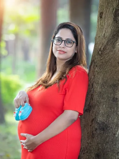 A close-up portrait holding tiny blue shoes. The soft light and natural background highlight the mom-to-be's gentle smile and happy glow.