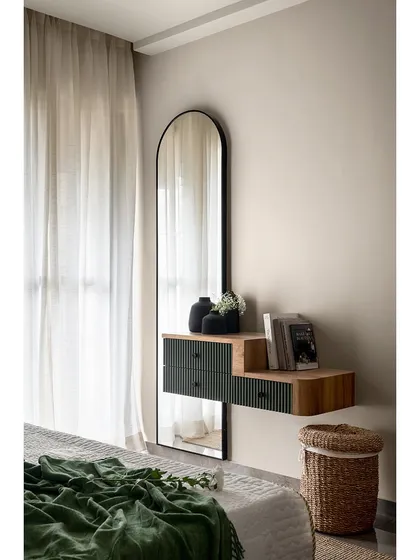 A detail shot of the master bedroom's dressing area. A floating console with fluted green drawers is paired with a full-length arched mirror, creating a functional and stylish vanity space.