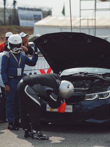 Racers in full gear perform last-minute checks under the hood of a BMW performance sedan. The attention to detail is everything.